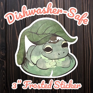 May include: A 3-inch frosted sticker featuring a cartoon frog wearing a hat and resting on a lily pad, under a large leaf. The sticker has the words "Dishwasher-Safe" and "Frosted Sticker" in a cursive font.