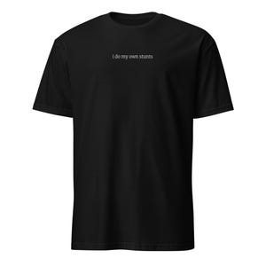 Może przedstawiać: Czarny t-shirt z białym napisem "i do my own stunts" pośrodku klatki piersiowej. Koszulka ma krótkie rękawy i okrągły dekolt.