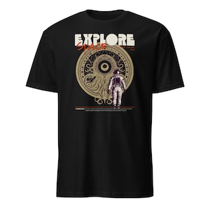 May include: Black t-shirt with a graphic design featuring the text "EXPLORE SPACE" above an illustration of an astronaut and a cosmic entity. The design is in shades of beige and brown.