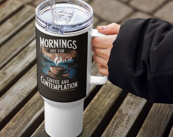 May include: White travel mug with a handle and a clear lid. The mug features the text "Mornings are for Coffee and Contemplation" with a graphic of a coffee cup, mountains, and a river. The mug is held by a person.