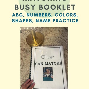May include: A personalized busy booklet with a black spiral binding. The cover features the text 'Oliver CAN MATCH!' above a small photograph of a child. The top text reads 'PERSONALIZED MATCHING BUSY BOOKLET ABC, NUMBERS, COLORS, SHAPES, NAME PRACTICE'.