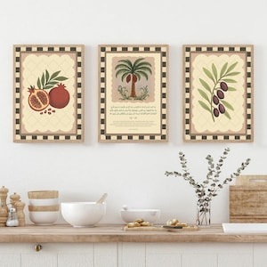 May include: Three framed art prints with botanical illustrations. One print features pomegranates, another a palm tree, and the third an olive branch. Each print has a beige background with a decorative border and a checkered frame.
