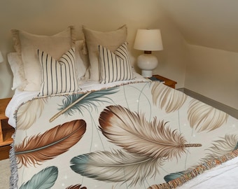 May include: A beige throw blanket with a large feather pattern in shades of brown, teal, and cream. The blanket is draped over a bed with matching pillows and a white bedspread. The room has a cozy, neutral color scheme.