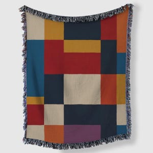 May include: A colorful throw blanket with a geometric design. The blanket features a patchwork of rectangles in various colors, including red, blue, yellow, orange, and beige. The edges are finished with a fringe.