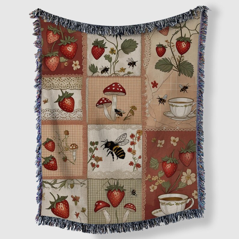 May include: A patchwork throw blanket with a design of strawberries, mushrooms, bees, and teacups. The blanket has a fringed edge and a colour palette of red, cream, and brown. The design evokes a vintage aesthetic.