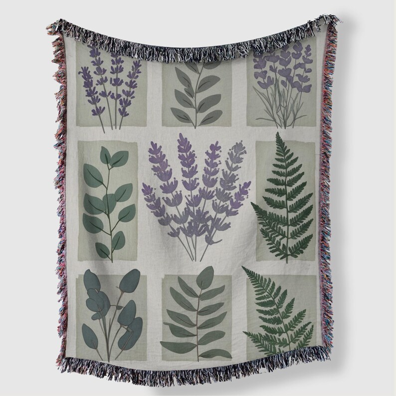 May include: A woven throw blanket with a botanical design. The design features illustrations of lavender, ferns, and other foliage in shades of purple and green, set against a light grey background. The blanket has a fringed edge.