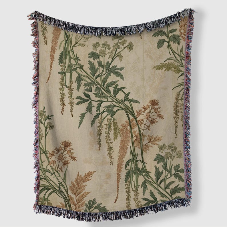 May include: A beige throw blanket with a botanical print featuring green, brown, and tan floral and foliage designs. The blanket has a fringed edge with a mix of colors, including blue, pink, and tan. The overall design has a vintage aesthetic.