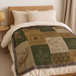 May include: A patchwork throw blanket with a nature theme, featuring deer, trees, and botanical designs in shades of green, brown, and beige. The blanket has a fringed edge and is displayed on a bed with cream-coloured bedding.