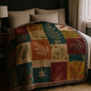 Könnte beinhalten: Eine Patchwork-Wurfdecke mit botanischem Design. Die Decke hat Quadrate in verschiedenen Farben, darunter Türkis, Rost und Gold, die jeweils mit Bildern von Blättern und Blumen verziert sind. Die Decke hat einen Fransenrand und ist über ein Bett drapiert.