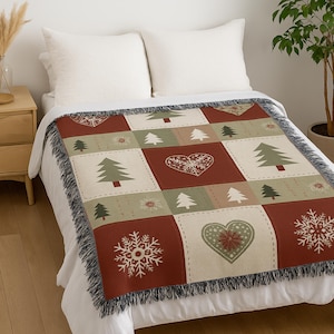 May include: A woven throw blanket with a patchwork design featuring Christmas trees, snowflakes, and hearts in red, green, and cream colors. The blanket has a fringed edge and is displayed on a bed.