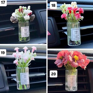May include: Four car air vent diffusers with small glass vases filled with colorful artificial flowers. Each vase has a label that reads "GOOD LUCK". The flowers are in shades of pink, red, white, and yellow.