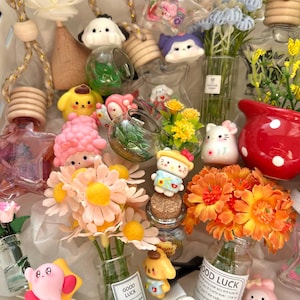 以下が含まれることがあります： 花、漫画のキャラクターのフィギュア、芳香剤など、装飾品のコレクション。 ピンク、黄色、オレンジ、白の色使いで、木製のアクセントと透明なガラスを使用。 一部のアイテムには「GOOD LUCK」の文字が入っています。