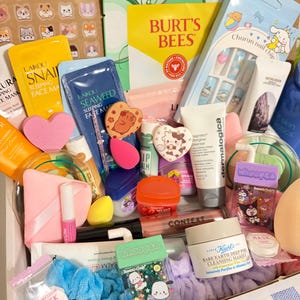 Op de afbeelding: Een verzameling schoonheidsproducten, waaronder gezichtsmaskers, lippenbalsems en huidverzorgingsartikelen. Het assortiment bevat producten van Burt's Bees, Kiehl's en Dermalogica, samen met stickers en nail art. De items zijn gerangschikt in een doos.
