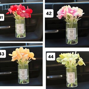May include: Four small glass vases, each containing a different color of artificial flowers. The flowers are red, pink, yellow, and light green. Each vase has a label that says "GOOD LUCK".