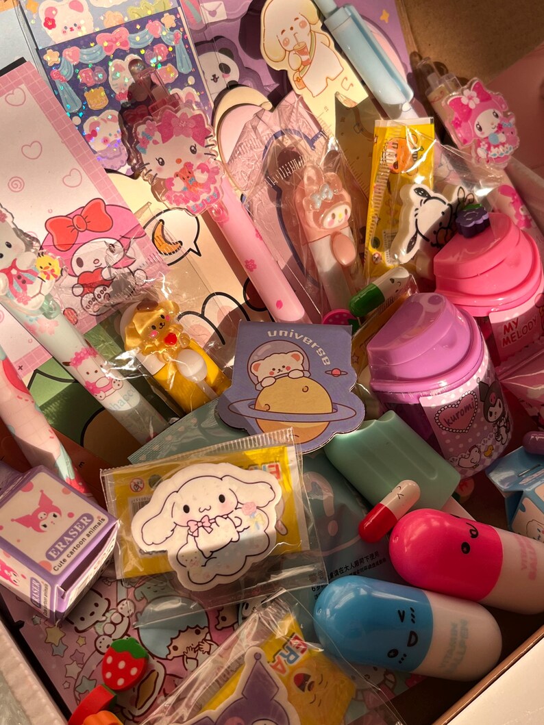 Op de afbeelding: Een verzameling kleurrijke briefpapier en accessoires, waaronder pennen, gummen, stickers en een paarse beker. De items bevatten stripfiguren en ontwerpen, met roze, blauwe en gele accenten. Het woord "universe" is zichtbaar op een sticker.
