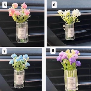 May include: A set of four car air vent diffusers, each featuring a small glass vase with artificial flowers. The vases have a ribbed design and a label that reads "GOOD LUCK". The flowers are pink, white, blue, and purple.