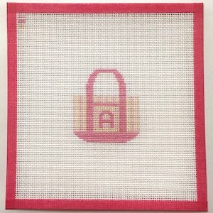 May include: A square needlepoint canvas featuring a white mesh grid with a pink border. Centered on the canvas is a stylized pink and yellow handbag graphic. The design is composed of small, uniform stitches, creating a clear, geometric pattern.