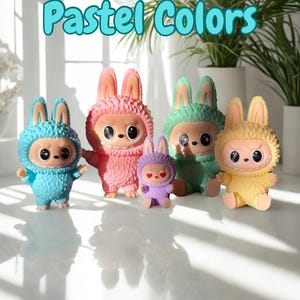 May include: A collection of colorful bunny-like figurines in pastel shades of blue, pink, green, purple, and yellow. Each figure has large eyes and a textured, furry appearance. The text "Pastel Colors" is displayed above the figurines.