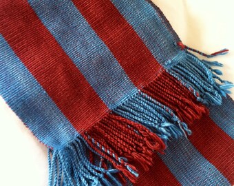 May include: A striped scarf with red and blue stripes and a fringe on the end.