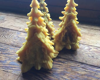 May include: Three yellow beeswax Christmas tree candles on a wooden surface.
