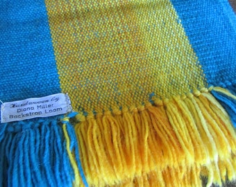 May include: Handwoven blue and yellow striped throw blanket with fringe. The blanket has a label that reads "Handwoven by Diana Miller Backstrap Loom".