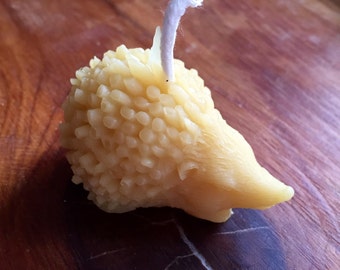 May include: A yellow beeswax candle shaped like a hedgehog with a white wick.