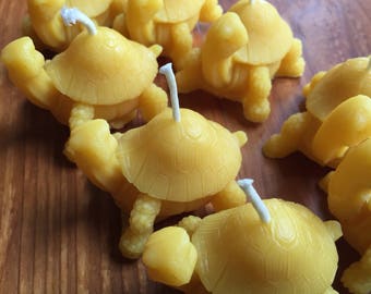 May include: A group of eight small, yellow beeswax candles shaped like turtles. Each candle has a white wick.