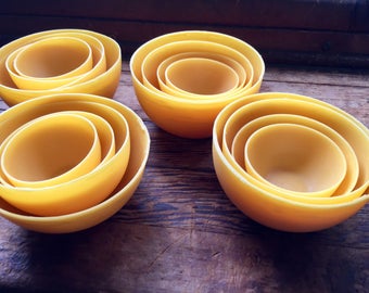 May include: Four sets of nesting bowls made of yellow ceramic. Each set has three bowls of different sizes, with the smallest bowl inside the largest.