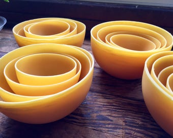 May include: Four sets of nesting bowls made of yellow beeswax. Each set has three bowls of different sizes.