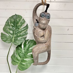 May include: A wooden monkey sculpture with a baby monkey in its arms. The monkey is carved with intricate details and has a gray-brown color.