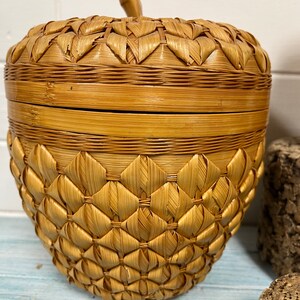 May include: A woven wicker basket shaped like an apple with a lid. The basket is made of natural brown and tan colored wicker.