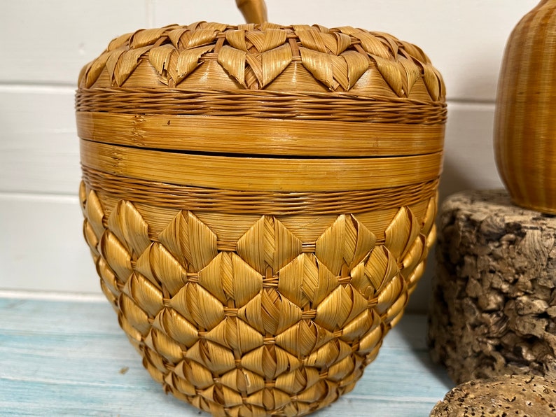 May include: A woven wicker basket shaped like an apple with a lid. The basket is made of natural brown and tan colored wicker.
