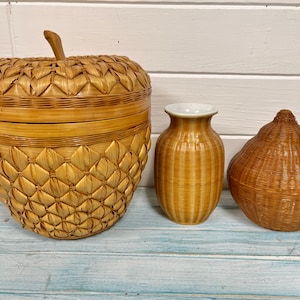 May include: Three woven baskets in different shapes and sizes. The largest basket is shaped like an apple and has a lid. The middle basket is a tall vase with a striped pattern. The smallest basket is pear-shaped.