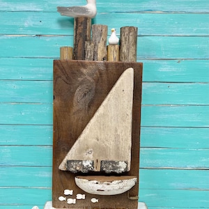 May include: A wooden sculpture of a sailboat with a white sail and a brown hull. The sailboat is surrounded by small white birds and fish. The sculpture is mounted on a wooden base.