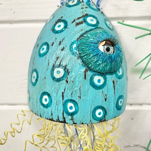 May include: A blue and white ceramic jellyfish with a large eye and a yellow wire tentacle. The jellyfish is decorated with white and blue eyes.