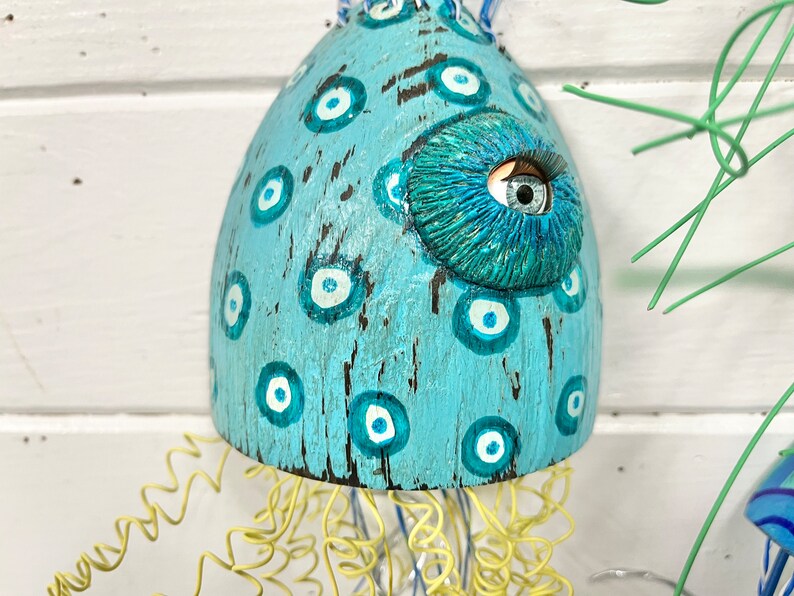 May include: A blue and white ceramic jellyfish with a large eye and a yellow wire tentacle. The jellyfish is decorated with white and blue eyes.