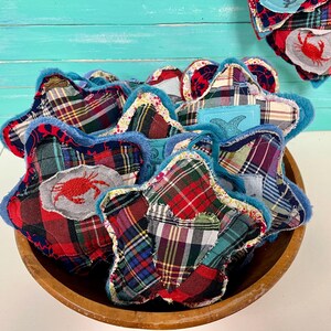 May include: A wooden bowl filled with star-shaped fabric ornaments. The ornaments are made from plaid fabric in red, green, and blue, with a blue trim. Some have a crab applique.