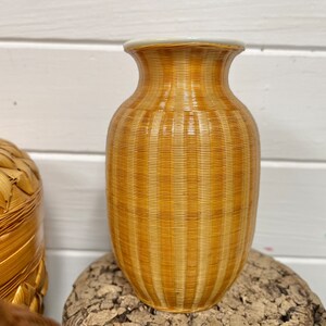 May include: A brown and white striped ceramic vase with a glossy finish. The vase is sitting on a piece of wood.