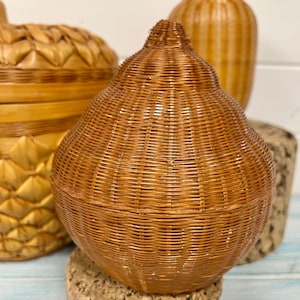 May include: Three woven wicker baskets in the shape of a pear, an apple, and a cylinder. The baskets are all made of natural brown wicker and have a rustic, handmade look.