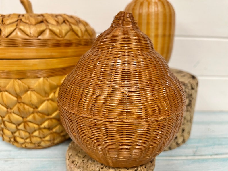 May include: Three woven wicker baskets in the shape of a pear, an apple, and a cylinder. The baskets are all made of natural brown wicker and have a rustic, handmade look.
