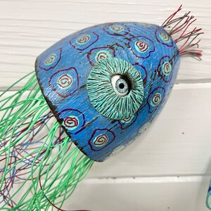 May include: A blue and green painted wooden jellyfish with a single white eye and a green wire mesh tentacle.