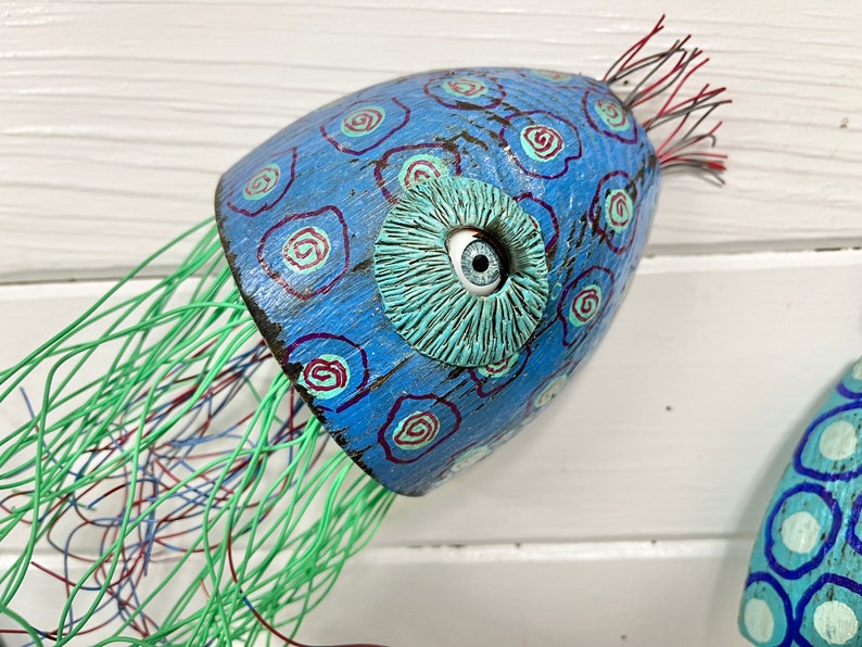 May include: A blue and green painted wooden jellyfish with a single white eye and a green wire mesh tentacle.