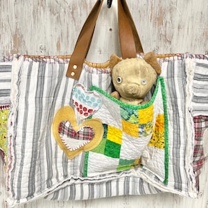 May include: A large tote bag with brown leather handles and a patchwork design. The bag features a striped pattern, decorative hearts, and a small stuffed animal peeking out of a pocket. The bag is made of quilted fabric.