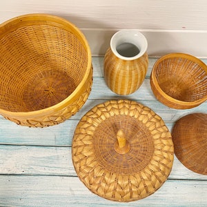 May include: A set of four woven baskets in various shapes and sizes. The baskets are made of natural materials and have a light brown color. The baskets are arranged on a light blue wooden surface.