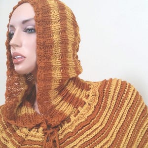 May include: A brown and yellow striped crocheted hooded poncho with a long, flowing design.