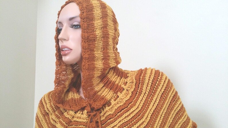 May include: A brown and yellow striped crocheted hooded poncho with a long, flowing design.