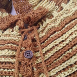 May include: A brown and beige crocheted shawl with a button closure and a tie at the neck.