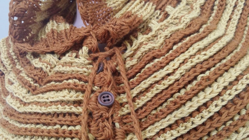 May include: A brown and beige crocheted shawl with a button closure and a tie at the neck.