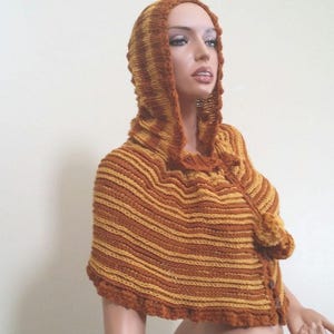 May include: A brown and yellow striped hooded knitted poncho with a pom-pom detail.