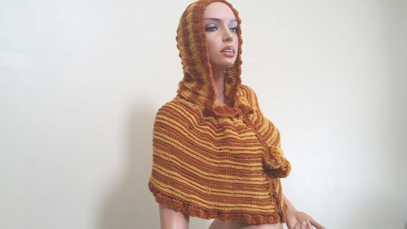 May include: A brown and yellow striped hooded knitted poncho with a pom-pom detail.